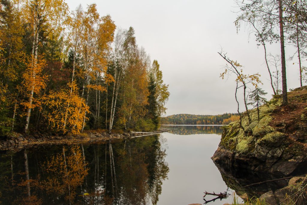 Syksyinen maisema jossa puissa ruskaa heijastuu tyyneen järven pintaan.